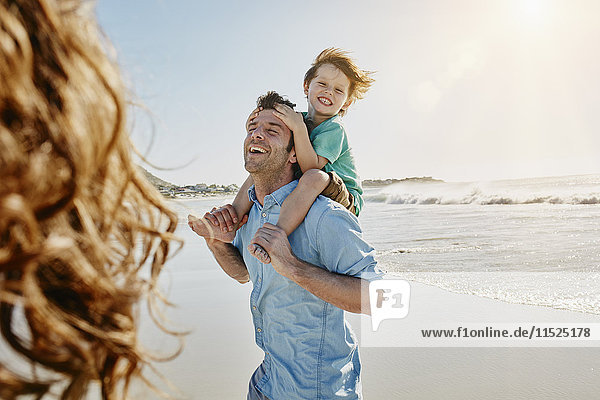 Vater trägt seinen kleinen Sohn auf den Schultern am Strand.