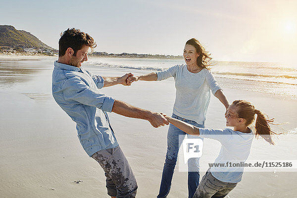 Couple playing with daughter ring-a-ring-a-roses on the beach