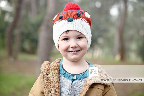 Porträt eines lächelnden Jungen mit Wollmütze im Wald