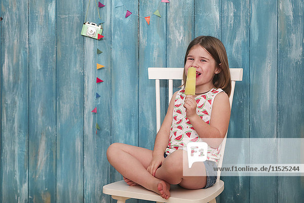 Fröhliches kleines Mädchen sitzt auf einem Stuhl und isst Zitroneneis.