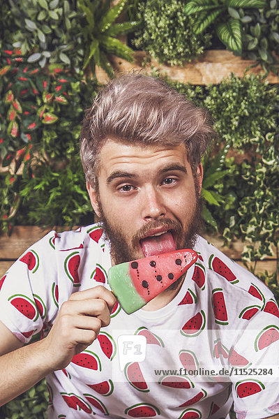 Portrait of young man eating watermelon ice lolly on terrace in front of vertical garden