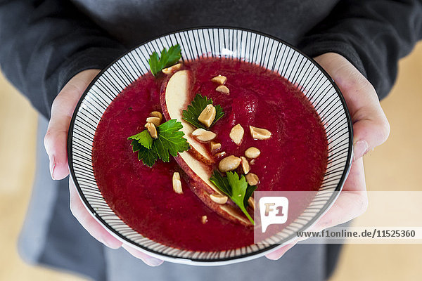 Mädchenhände mit Rote-Beete-Suppe  garniert mit Apfelscheiben  Erdnüssen und glatter Petersilie