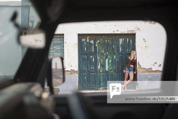 Spanien  Teneriffa  junge blonde Frau an der Wand vor einer Holztür lehnend