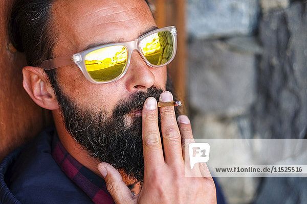 Porträt eines Mannes mit verspiegelter Sonnenbrille  der Zigarillo raucht.