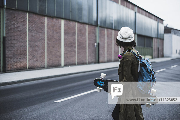 Junge Frau mit Kopfhörer  Rucksack und Skateboard auf der Straße