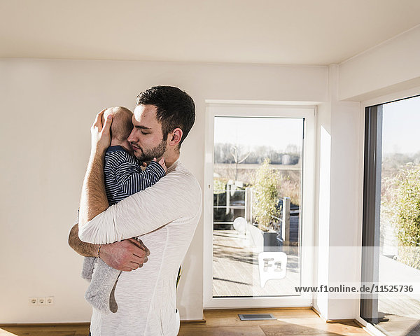Vater hält und umarmt seinen kleinen Sohn,  steht im gemütlichen Heim