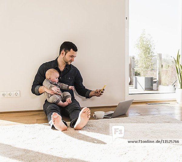 Father with baby son reading messages sitting on floor