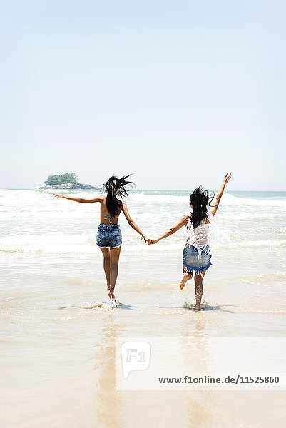 Brasilien  Sao Paulo  Ubatuba  zwei junge Frauen  die am Strand rennen und Händchen halten.