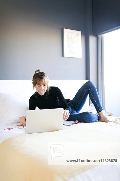 Junge Frau auf dem Bett liegend mit Laptop
