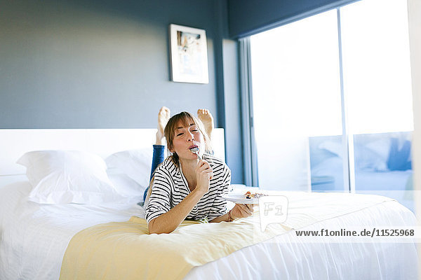 Young woman eating piece of vegan cake  lying on bed  licking spoon