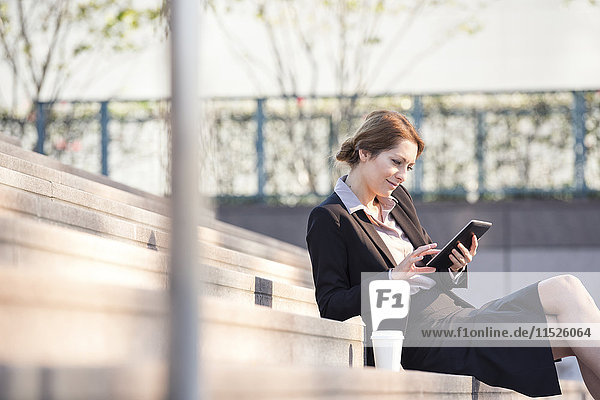 Businesswoman sitting on stairs using tablet