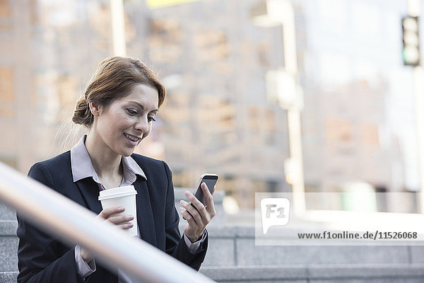 Lächelnde Geschäftsfrau mit Handy und Kaffee zum Mitnehmen