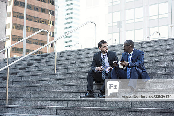 Zwei Geschäftsleute sitzen auf einer Treppe und reden.