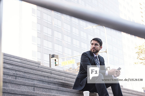 Businessman sitting on stairs with cell phone and takeaway coffee