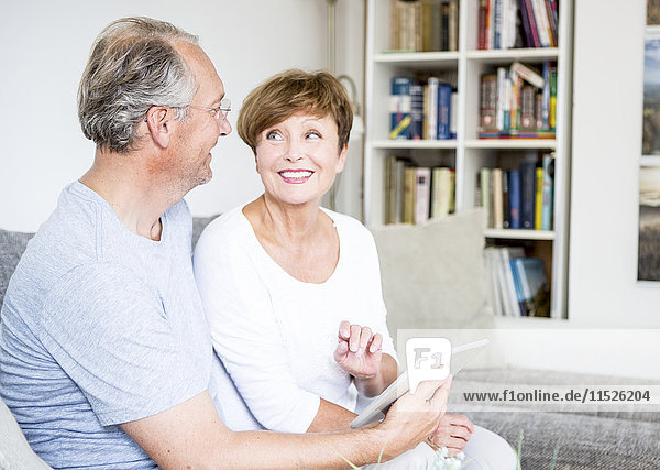 Senior couple at home sitting on couch using digital tablet