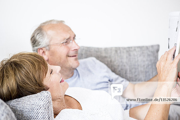 Senior couple at home lying on couch using digital tablet