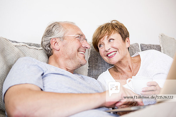 Happy senior couple at home sitting on couch using laptop