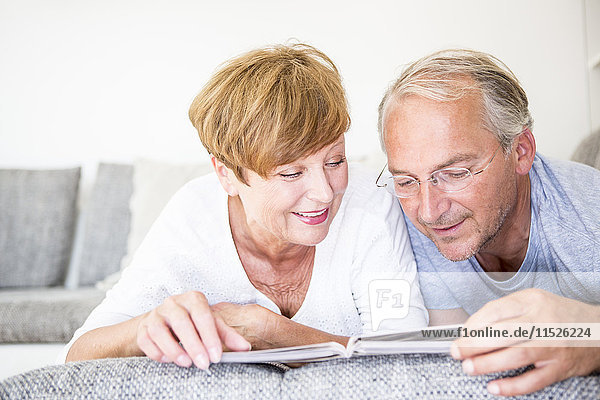 Senior couple at home lying on couch looking at photo album