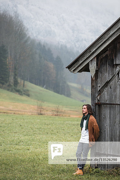 Österreich  Mondsee  junger Mann an einer Holzhütte auf einer Wiese gelehnt