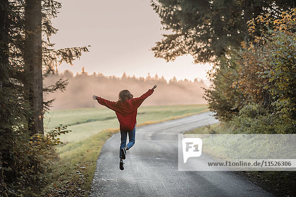 Back view of woman jumping with arms outstretched on country road in the evening