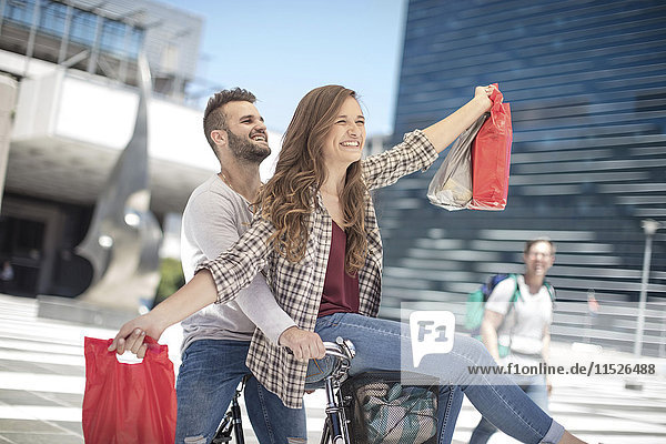 Fröhliches junges Paar beim Fahrradfahren in der Stadt mit Einkaufstaschen