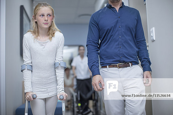 Girl with crutches walking with father in hospital