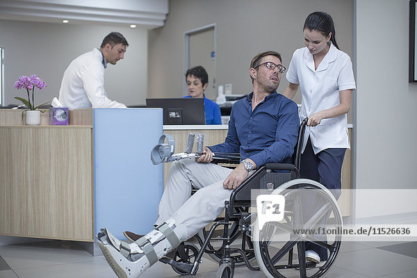 Krankenschwester schiebt Patient im Rollstuhl durchs Krankenhaus