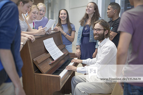 Lehrer mit einer Gruppe von Schülern  die um das Klavier herum stehen.