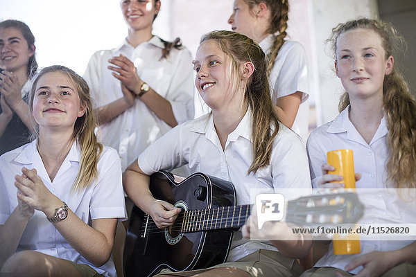 Female high school student playing guitar with group of school friends outside
