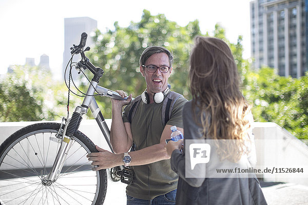 Junge Frau im Gespräch mit jungem Mann  Fahrrad auf der Schulter tragend