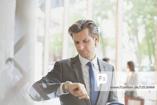 Businessman checking the time on wristwatch in office lobby