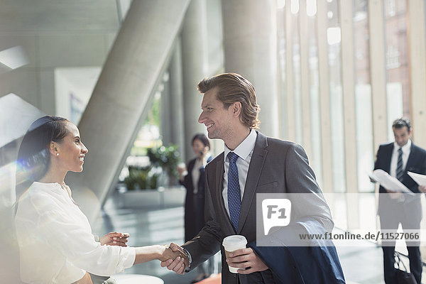Businessman and businesswoman handshaking in sunny office lobby