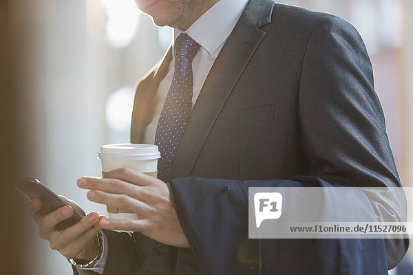Close up businessman in suit with coffee texting with cell phone