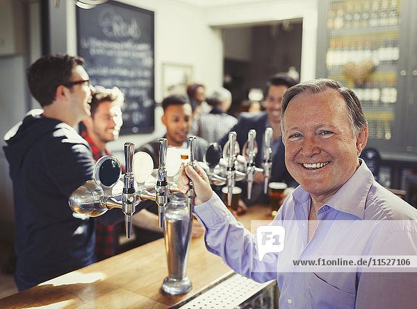 Portrait smiling male bartender standing at tap behind bar