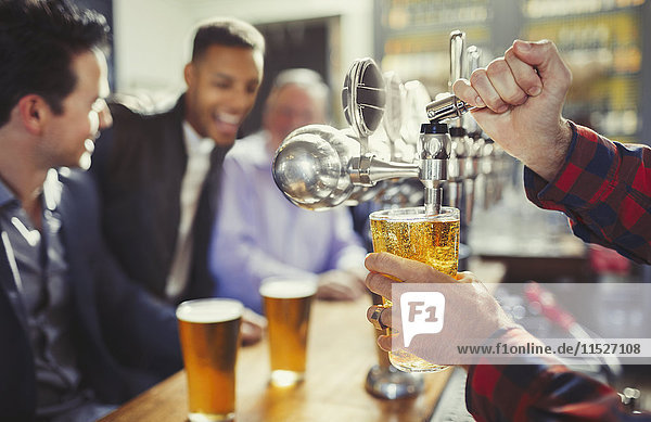 Barkeeper gießt Bier aus dem Schankhahn hinter der Bar