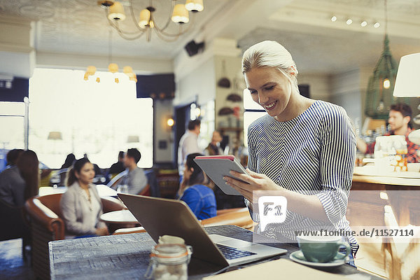 Lächelnde kreative Geschäftsfrau mit digitalem Tablett und Laptop im Cafe