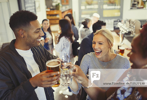 Laughing friends toasting beer and wine glasses at bar