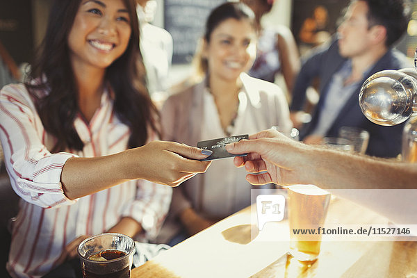 Lächelnde Frau bezahlt Barkeeper mit Kreditkarte an der Bar