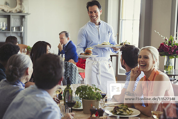 Smiling waiter serving food to friends dining at restaurant table