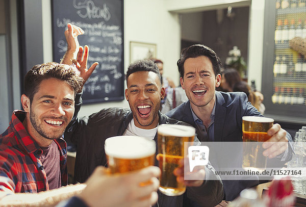 Portrait enthusiastic men friends toasting beer glasses at bar