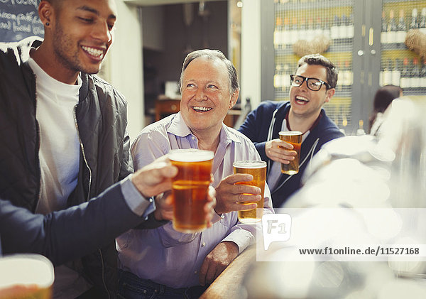Smiling men friends toasting beer glasses at bar