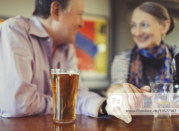 Seniorenpaar hält Händchen und trinkt Bier an der Bar.