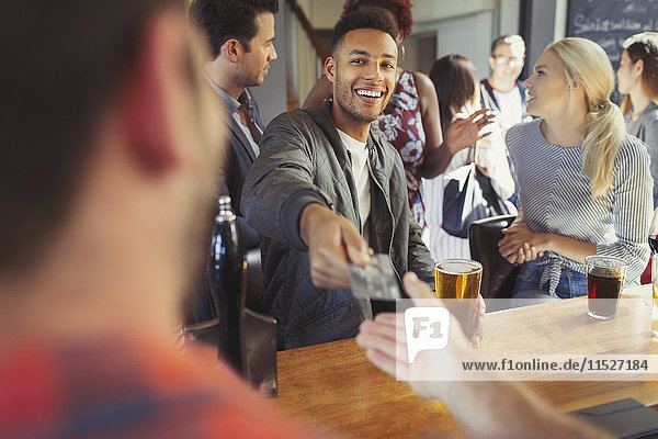 Lächelnder Mann bezahlt Barkeeper mit Kreditkarte an der Bar