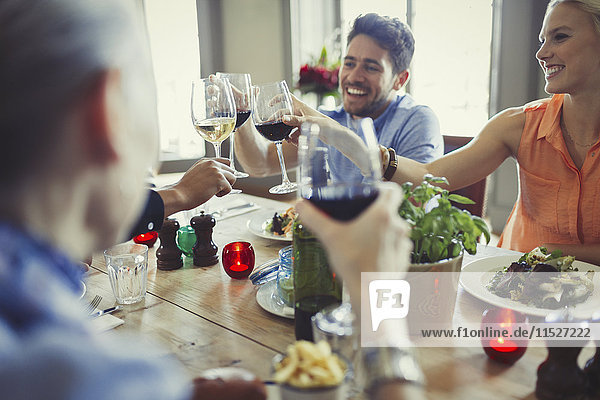 Smiling friends celebrating  toasting wine glasses at restaurant table