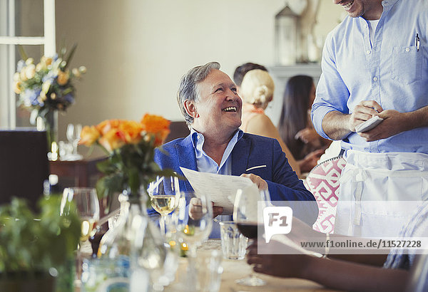 Smiling man with menu ordering from waiter at restaurant table