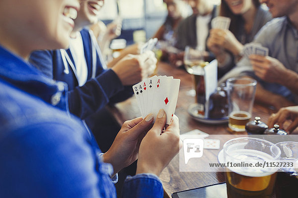 Frau hält Asse, spielt Poker und trinkt Bier mit Freunden am Tisch in der Bar.