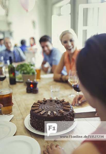 Woman cutting chocolate birthday cake with friends at restaurant table