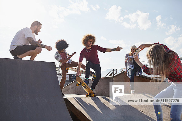 Frau fotografiert männliche Freunde beim Skateboarden auf der Rampe im sonnigen Skatepark.