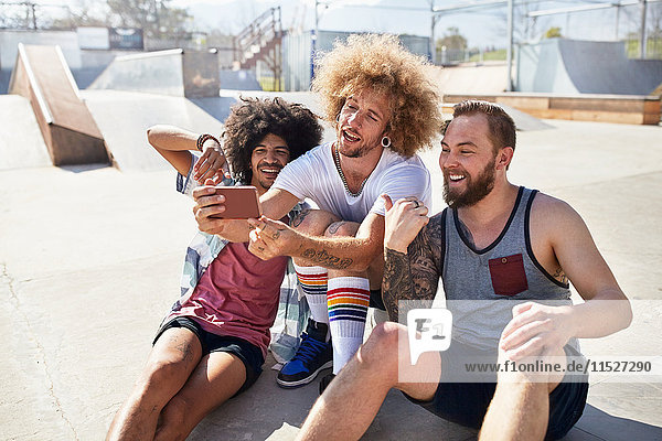 Männliche Freunde mit Fotohandy beim Selfie im sonnigen Skatepark