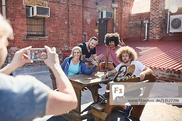 Frau mit Fotohandy fotografiert Freunde  die auf dem sonnigen Stadtdach rumhängen.